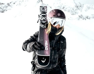 Power Ski - Frau mir Skihelm und Skibrille trägt Damen Ski auf Schulter