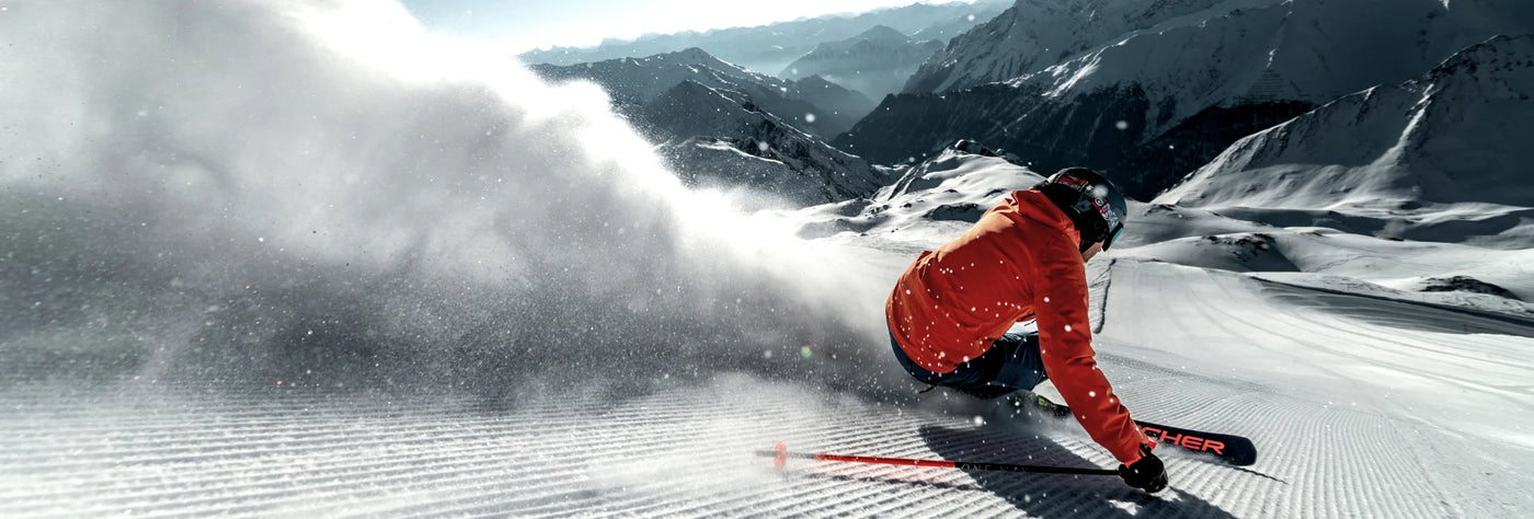 Power Ski - Mann mit Skihelm und oranger Skijacke wirbelt Schnee bei Schwung auf